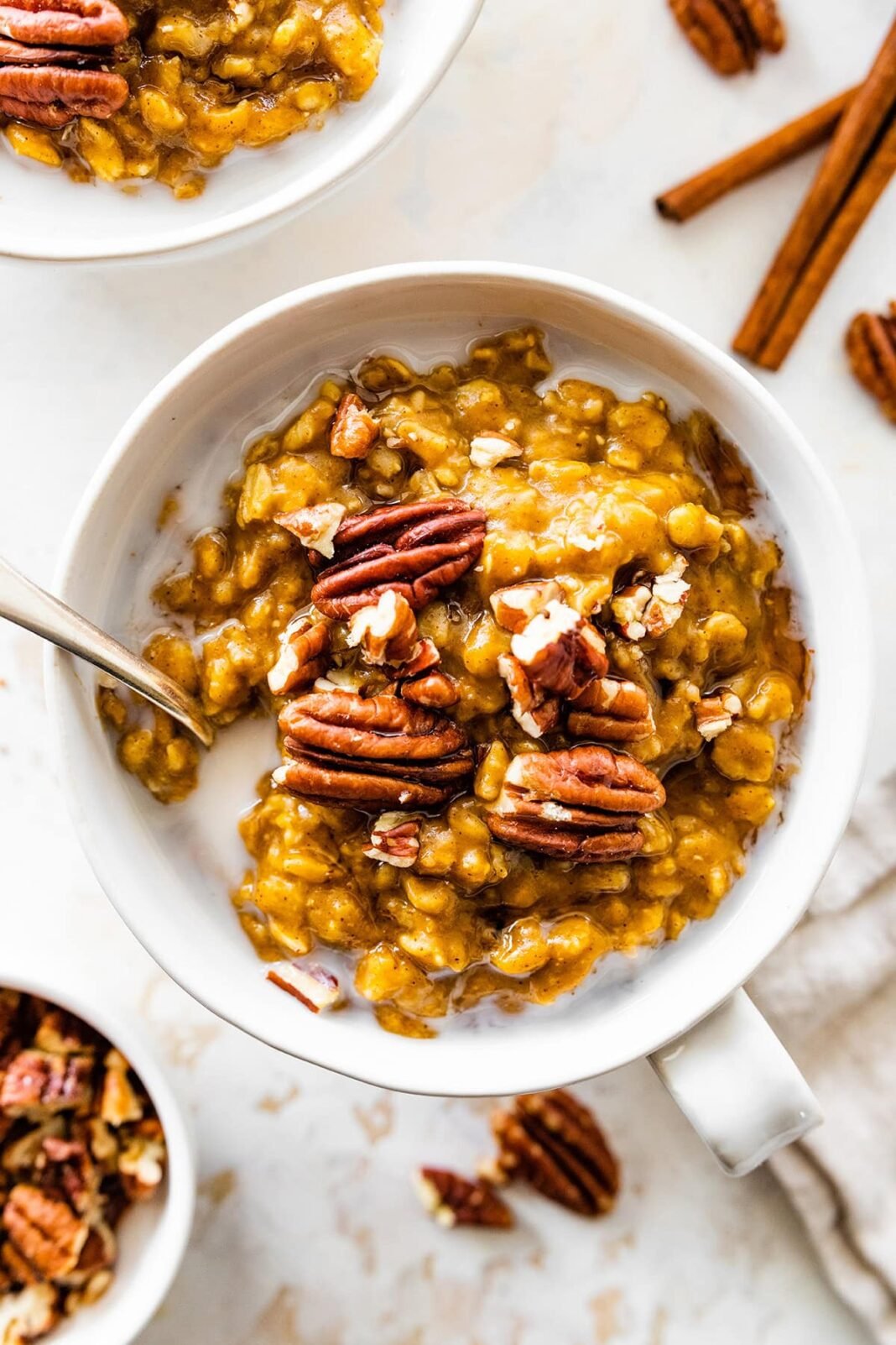 A bowl of pumpkin oatmeal with milk, and topped with pecans.