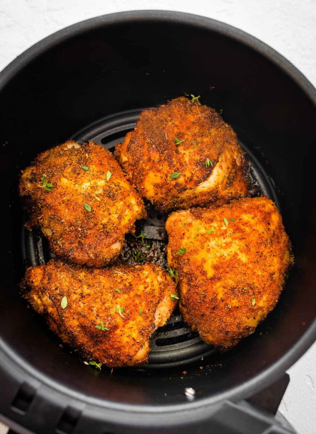 Four bone-in chicken thighs cooked in the basket of an air fryer topped with fresh parsley.