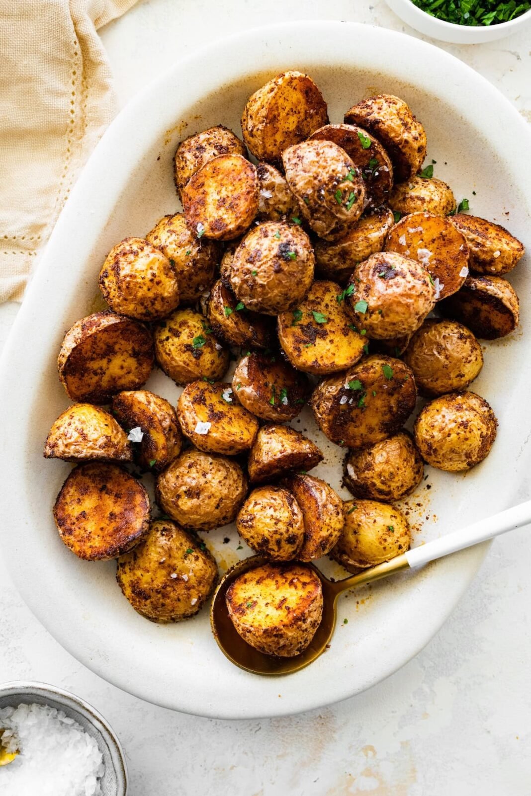 Crispy air fryer potatoes on a white plate garnished with fresh herbs and flaky sea salt.