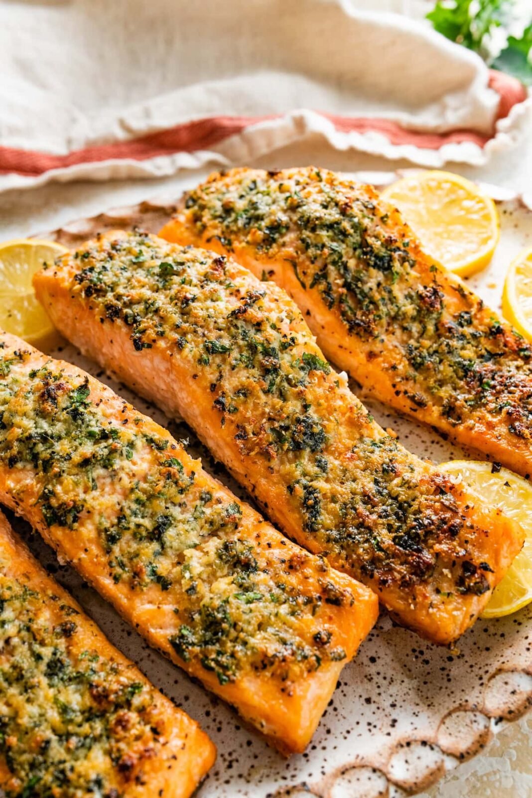 Four parmesan crusted salmon filets served on a speckled tray with multiple lemon slices.