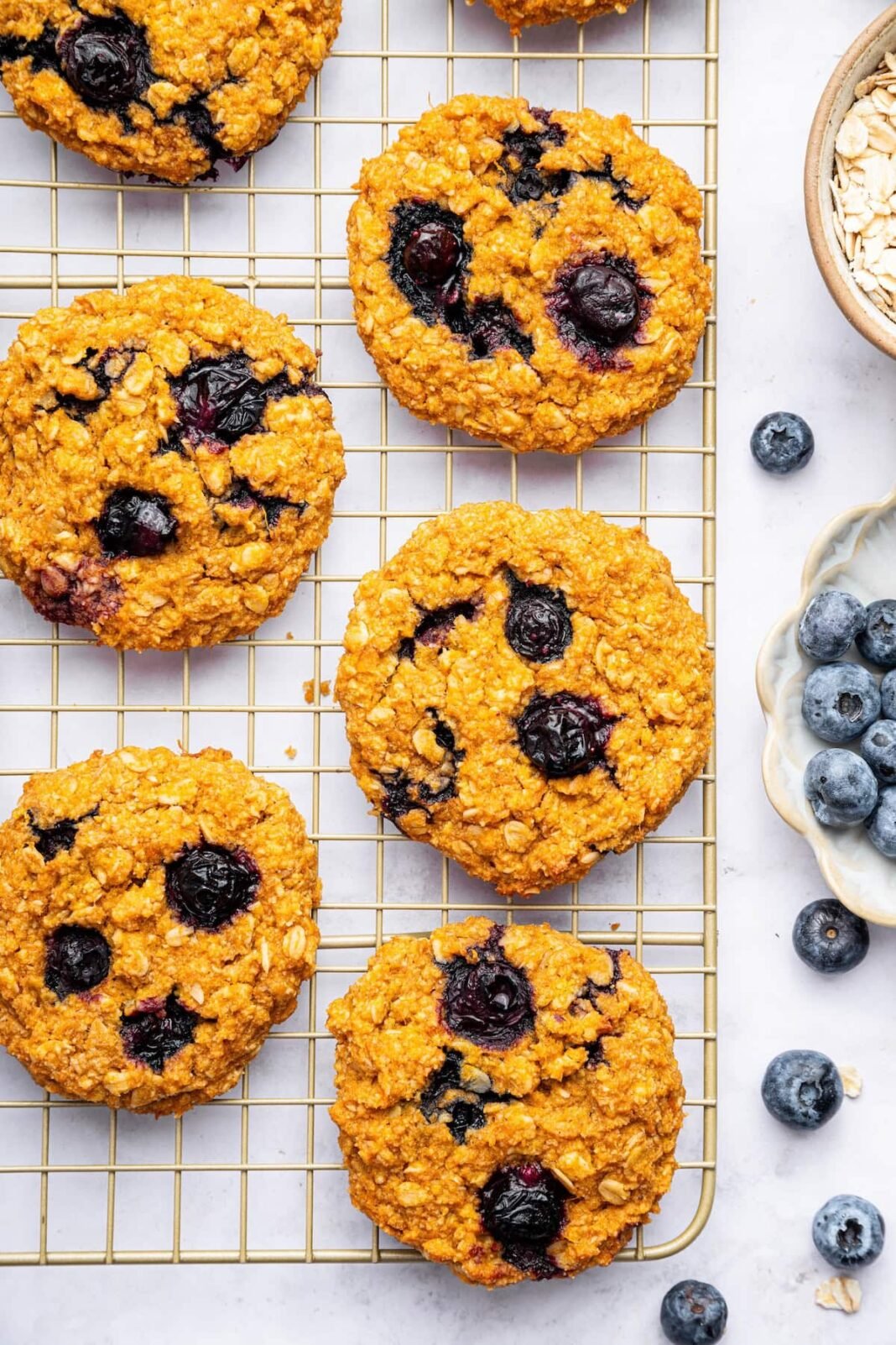 Six sweet potato blueberry oatmeal cookies on a wire cooling rack. Fresh blueberries are scattered next to the rack.